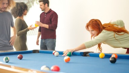 Woman hitting a ball playing pool with friends at home