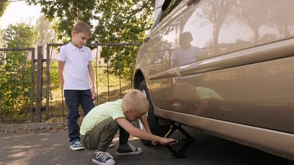 Children repair the car, lift the car with a jack and change the wheel. Two brothers play adult car mechanics and change the wheels on Dad's car.