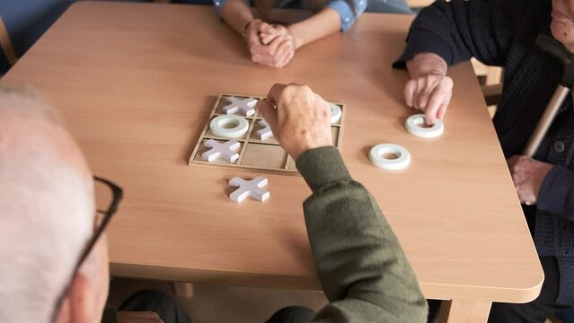 Senior friends playing tic tac toe at table in nursing home