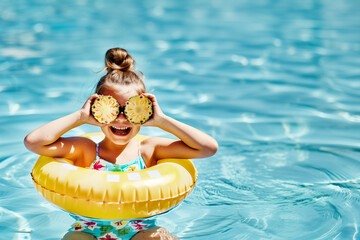 girl in swimming pool playing with pineapple slices - obrazy, fototapety, plakaty