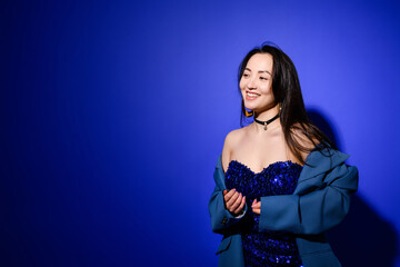 Cheerful asian woman in dress and choker standing on blue background 