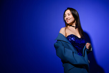 Stylish asian woman in evening outfit posing on blue background 