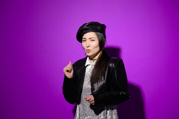 Stylish asian woman with facial expression looking at camera on purple 