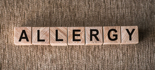 Wooden letter blocks arranged to spell ALLERGY on a wooden background.