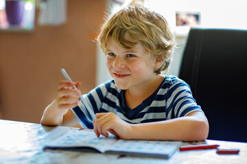 Portrait of happy boy doing homework in kitchen at home. Elementary school studing writing and...