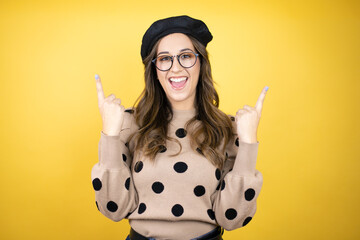 Young beautiful brunette woman wearing french beret and glasses over yellow background amazed and...