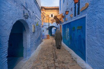 Man walking on narrow street in medina of blue city, Chefchaouen. Man wearing traditional clothes...
