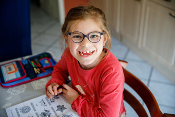 Portrait of happy little girl doing homework at home. Elementary school studing writing and...