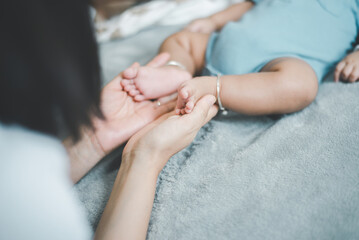 Mom hands holding baby feet lying on a comfortable bed at home,Newborn child - obrazy, fototapety, plakaty