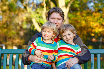 Two little kid boys and young father sitting together in colorful clothing on bench. Cute healthy...