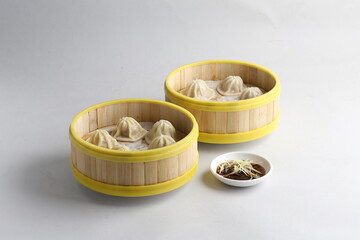 handmade steamed Shanghai Xiao long bao pork meat mini dumpling soup in bamboo basket on white table fast food asian snack dim sum halal food appetiser hotel restaurant banquet cuisine cafe menu