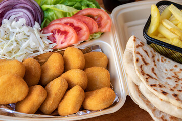 A tasty wrap sandwich featuring a medley of crisp onion, golden French fries, fresh green salad, and ripe tomato, all wrapped in a soft tortilla. Served with chicken nuggets on the side.