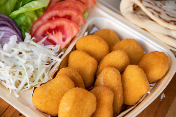 A tasty wrap sandwich featuring a medley of crisp onion, golden French fries, fresh green salad, and ripe tomato, all wrapped in a soft tortilla. Served with chicken nuggets on the side.