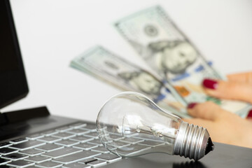 A girl counts dollars against the background of an incandescent light bulb and a laptop