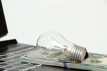 Incandescent lamp lies on dollars on laptop, high price of electricity, buy light
