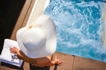 A rear view of tourist woman wearing a white hat is sitting near the spa jacuzzi. summer holidays