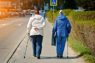Senior women walks with cane along the city streets, strolling together. Companionship in aging....