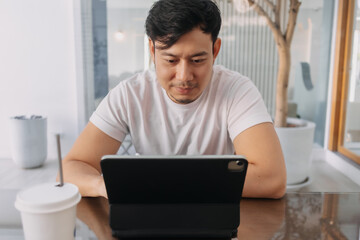 Front view of asian man using laptop, sitting and working at cafe, digital nomad and freelance concept.