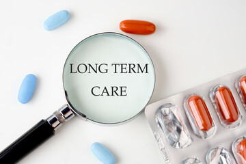 Medical concept. LONG TERM CARE text through a magnifying glass on a white background next to...