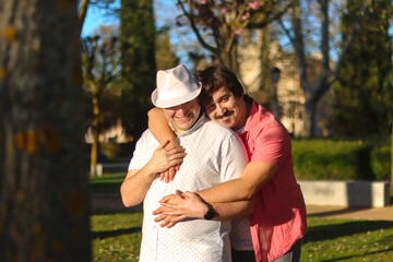 Couple of gay men hugging each other standing with natural park in the background on a sunny day....