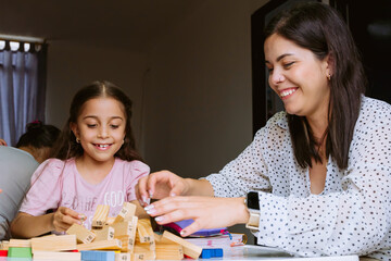 International Children Day and Family Day. Latin mother having fun with her children at *home* with blocks on white table. Single mother of two young children, responsible and happy. Concept of love. - obrazy, fototapety, plakaty