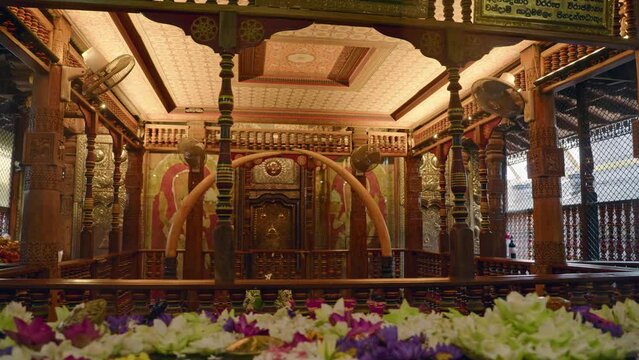Interior views intricate woodwork, golden hues inside Sri Dalada Maligawa, Kandy. Sacred chamber houses revered Buddha Tooth relic, surrounded by vibrant flowers, symbols of spirituality, worship.