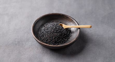 Black sesame seeds in a wooden bowl on a dark background.