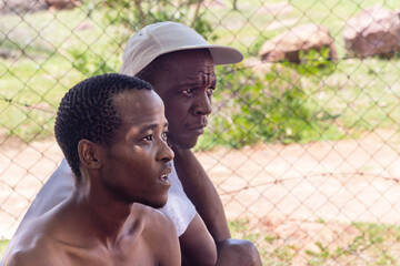 village african men having a talk in the yard outdoors, wire mesh fence in the background
