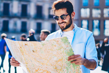 Happy bearded casual dressed tourist in stylish sunglasses enjoying adventure trip and reading man...