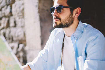 Cropped image of pondering bearded tourist in black sunglasses.Thoughtful male traveler dressed in...