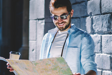 Cheerful bearded tourist happy to find right route strolling with coffee to go on streets of...