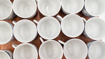 A row of white cups with blue designs sit on a wooden table