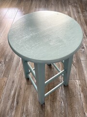 A wooden bar stool that's painted green. The images is taken from above at an angle and the pattern...