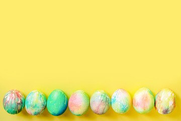 Easter brightly decorated pastel eggs in delicate blue, green, pink, yellow colors lie on a yellow background with space for text