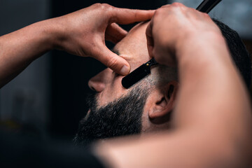 A man is getting his beard shaved by a barber. Side view.