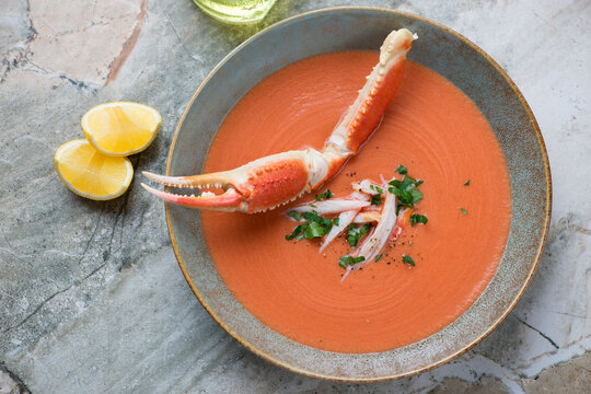Plate of bisque served with a boiled crab claw, horizontal shot on a grey granite surface, high angle view