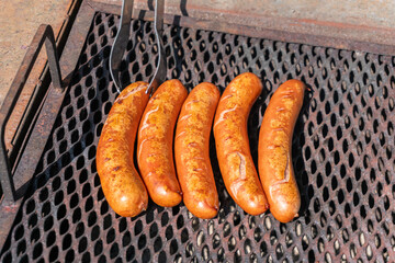Big yummy sausages are being grilled outdoors on a warm sunny day