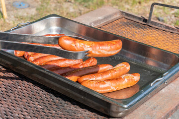 Big yummy sausages are being grilled outdoors on a warm sunny day