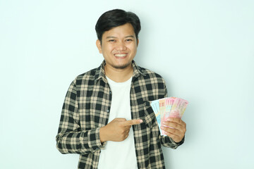 Young Asian man holding paper money while pointing his right finger at the money and smiling