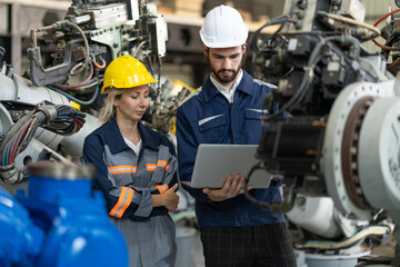 Male and female engineers with laptop checking and maintaining robot arm welding machine at...
