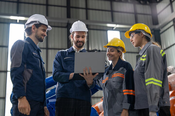 A diverse group of smiling industrial professionals collaborates over a laptop on the factory...