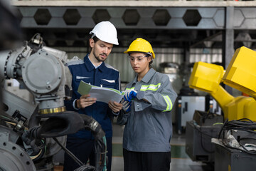 Two focused engineers, a man and a woman, consult a technical document in an industrial setting,...