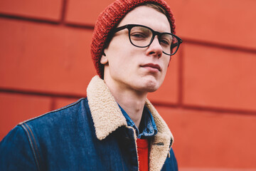 Half length portrait of serious hipster guy dressed in stylish denim jacket and red hat looking at...