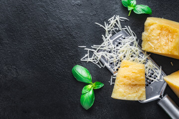 Parmesan cheese slices with basil leaves and grater on a dark stone background with copy space top view