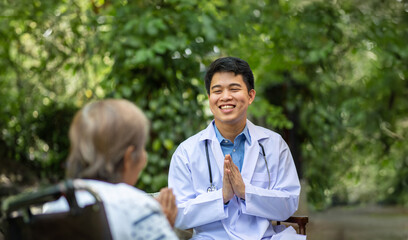 Thai doctor greeting elderly woman in nursing home.  Wai is the thai greeting(putting palms together).