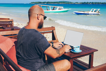 Skilled male freelancer working online on his business via laptop computer while resting on ocean...
