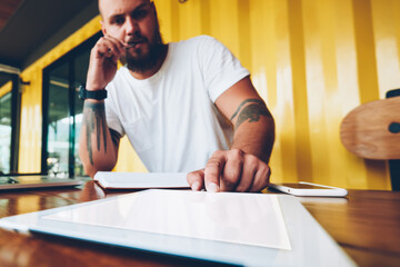 Serious hipster guy puzzled on idea for new online project pressing button on portable pc for...