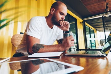 Thoughtful male student concentrated on doing homework task pondering on idea sitting at desktop...