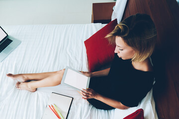 Top view of female blogger holding portable pc with blank screen resting on bed, young woman making...
