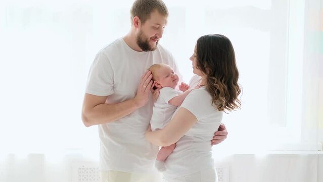 A happy young family mom dad and a small child smiling and kissing on a white isolated window background, a loving family threesome at home